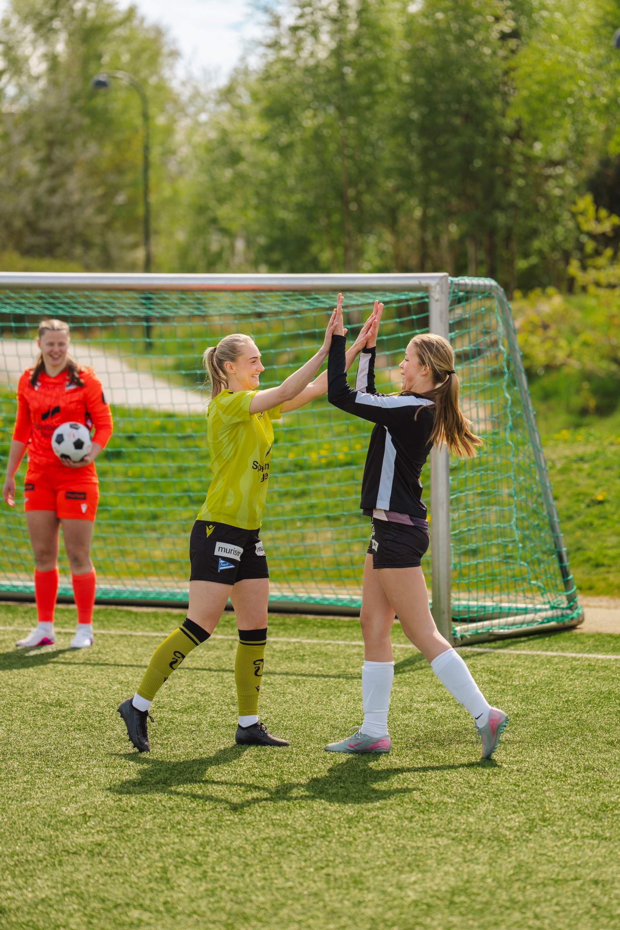 Fotballjenter tar highfive foran fotballmålet