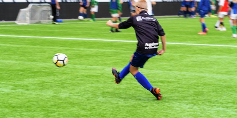 Gutt som sparker fotball på fotballbane
